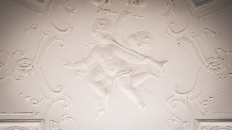 Detail from an ornamental relief ceiling within the ViCAS premises, showing two cherubs playing musical instruments.